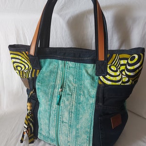 Peut inclure: Un sac cabas en denim bleu turquoise avec des accents en denim noir et une fermeture éclair. Le sac a des anses en cuir marron et une doublure en tissu à motifs jaunes et noirs.