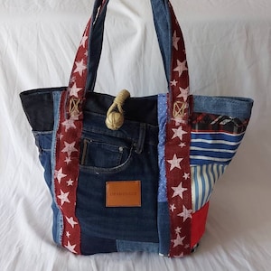 Peut inclure: Sac fourre-tout en denim patchwork avec des sangles rouges à étoiles blanches et une poignée en corde. Le sac présente divers délavages de denim et motifs de tissu, avec des accents rouges, blancs et bleus. Une étiquette en cuir marron avec "OBAMEBAGS" est cousue sur le devant.