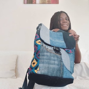 May include: A blue denim backpack with a colorful fabric panel and a black flap. The backpack is made from recycled denim and has a unique patchwork design.