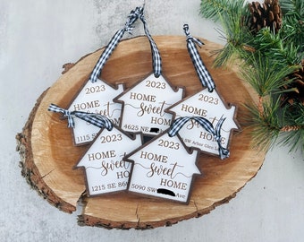 May include: Five wooden house-shaped ornaments with black and white checkered ribbon. Each ornament has the text "Home Sweet Home" and the year "2023" with a different address on each ornament.