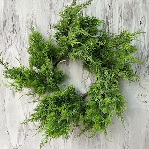 May include: A vibrant green wreath made of faux evergreen branches. The wreath is circular, with the branches arranged to create a full, textured appearance. The bright green color adds a touch of nature to any space.