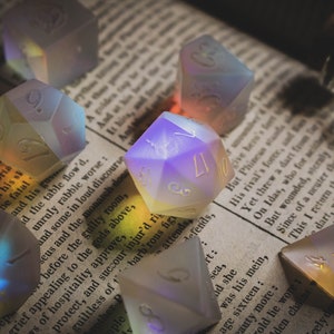 May include: A collection of iridescent dice with various numbers on each face, resting on a vintage book with text. The dice are made of a translucent material that shimmers with rainbow colours.