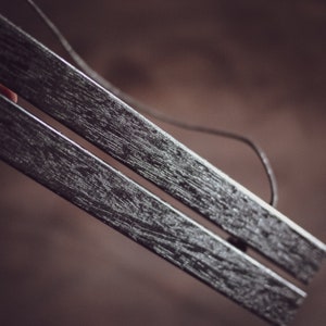 May include: Close-up of two dark gray wooden magnetic poster hangers. The wood grain is visible, and a thin string is attached for hanging. The background is a blurred brown.