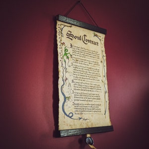 May include: A framed parchment scroll titled "Soul Contract" hangs against a burgundy wall. The scroll features ornate calligraphy, decorative borders with green and blue accents, and a wax seal. The wooden frame is dark brown.