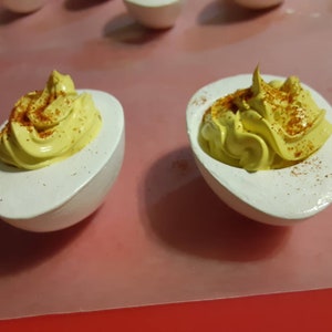 May include: Two white deviled eggs with yellow yolk filling and a sprinkle of red paprika on top.