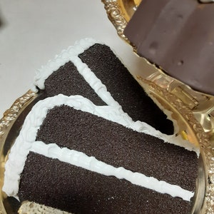 May include: A three-layered chocolate cake with white frosting on a gold tray. The cake is decorated with white frosting and has a crumbly texture.