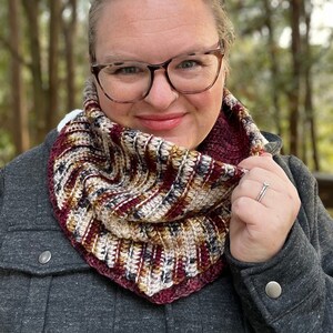 May include: A woman wearing a gray jacket with a brown, white, and burgundy crocheted infinity scarf. She is wearing glasses and has her hair pulled back.