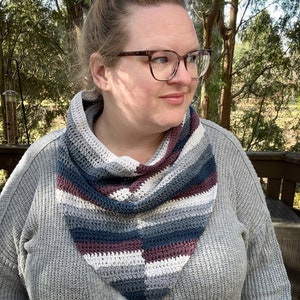 Könnte beinhalten: Ein grauer Häkel-Schal mit Streifen in Weiß, Grau, Blau und Burgunderrot.