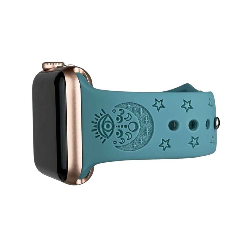 May include: A teal blue silicone watch band with a rose gold watch case. The band has a moon and eye design with stars.