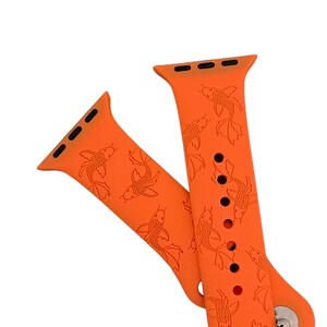 May include: Orange silicone Apple Watch band with a pattern of orange koi fish. The band has black accents and a black buckle.
