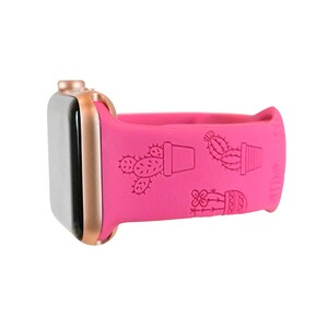 Pu&ograve; includere: Un cinturino per Apple Watch in silicone rosa con quadrante in oro rosa. Il cinturino presenta un design a cactus con diversi cactus in vaso.