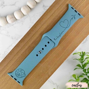 May include: A light blue silicone Apple Watch band with a globe and airplane design. The band has the text "...explore" engraved on it.