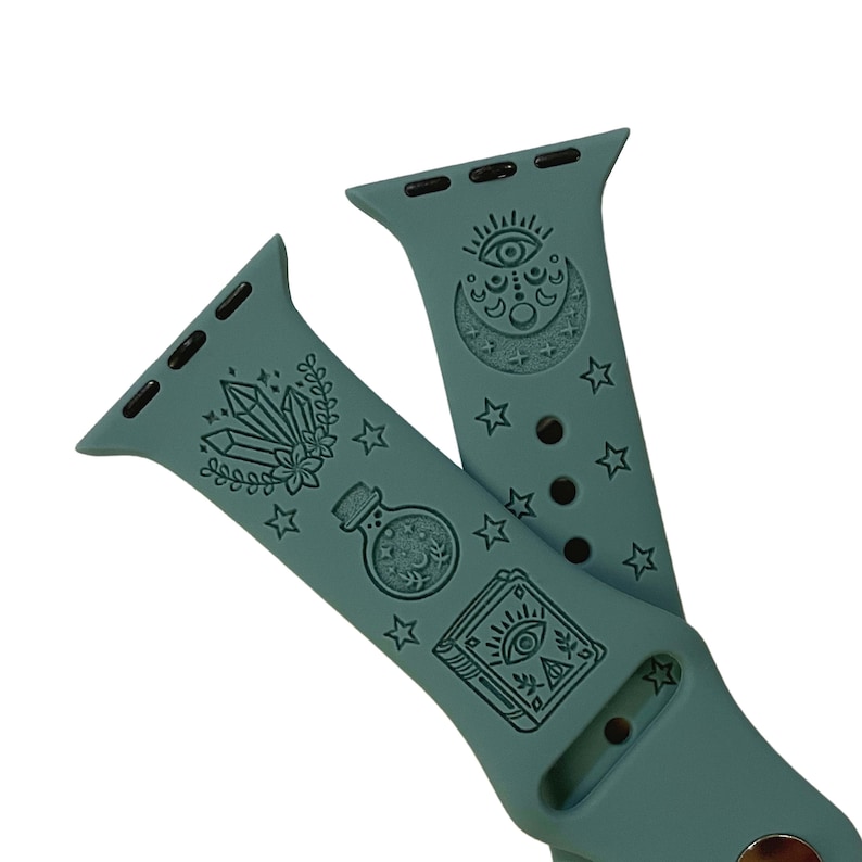 May include: A teal blue Apple Watch band with a mystical theme. The band features an eye, moon, stars, crystals, a potion bottle, and a book with an eye on the cover.