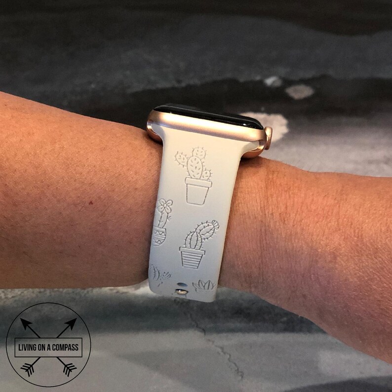 Pu&ograve; includere: Un cinturino bianco per Apple Watch con quadrante in oro rosa e un design a cactus. Il cinturino presenta una variet&agrave; di diversi design di cactus, tra cui un cactus in vaso, un cactus con fiori e un cactus con un singolo stelo.