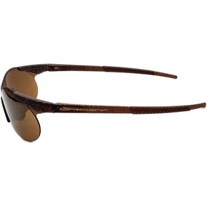 May include: Brown and gold-toned Oakley sunglasses with a textured frame and brown lenses.