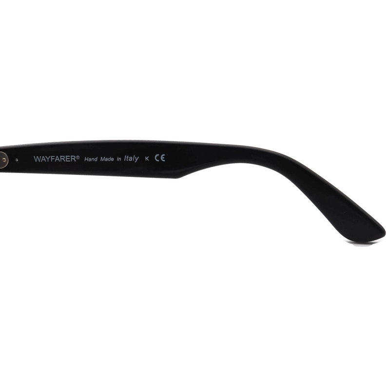 May include: Close-up of the black plastic arm of a pair of Wayfarer sunglasses. The arm is inscribed with the text "WAYFARER&reg; Hand Made in Italy K CE".