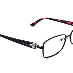May include: Black rectangular eyeglasses with a thin metal frame. The arms of the glasses are black with a pink and white tortoiseshell pattern. The brand name "VOGUE" is printed on the arm of the glasses.