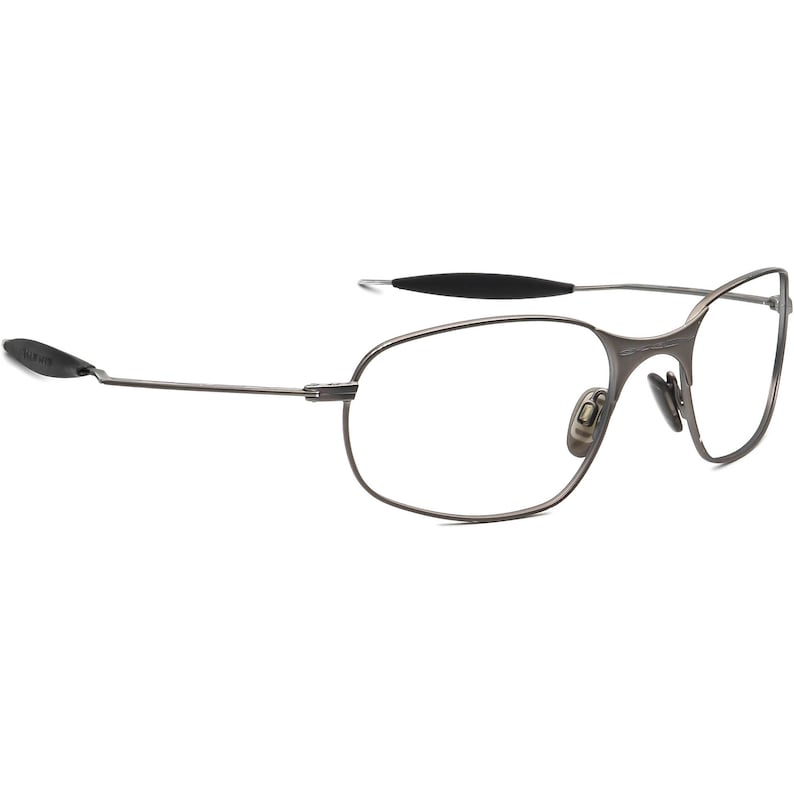 May include: A pair of rimless eyeglasses with a dark gray metal frame. The lenses are clear, and the temples have black rubberized ear pieces. The nose pads are also a light gray color.