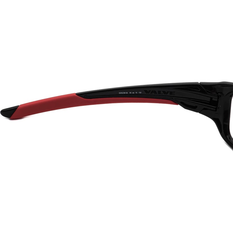 May include: Black and red sports sunglasses with the word "VALVE" printed on the side. The sunglasses have a red rubber temple arm and the text "DC2042 60 16 130" printed on the arm.