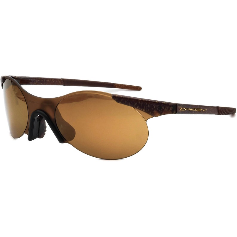May include: Brown and gold Oakley sunglasses with a brown frame and brown lenses. The sunglasses have a curved shape and a thin, gold-coloured Oakley logo on the right temple.