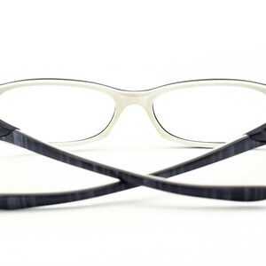 May include: White and black eyeglasses with a thin frame and black temples. The temples have a subtle wood grain pattern.