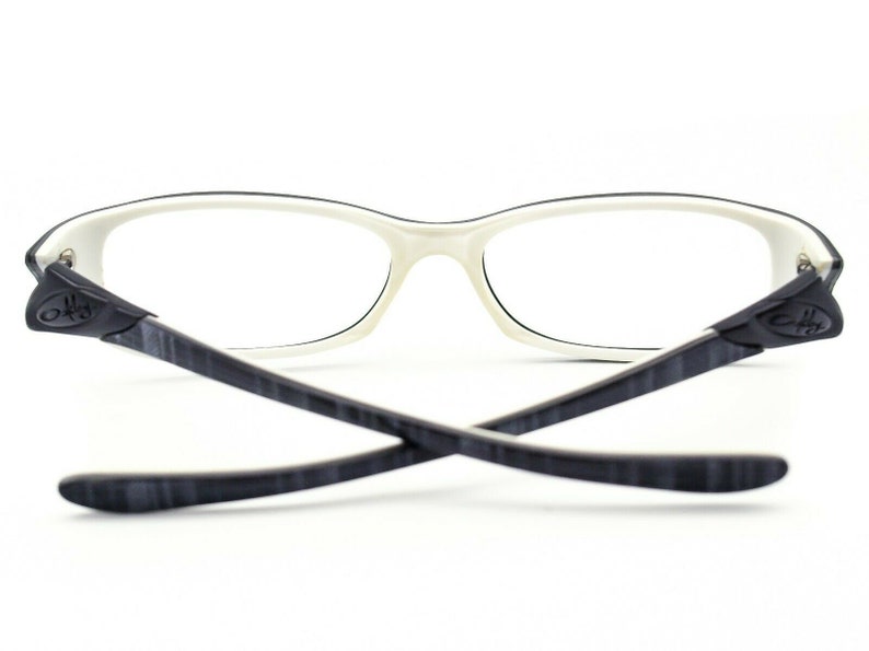 May include: White and black eyeglasses with a thin frame and black temples. The temples have a subtle wood grain pattern.