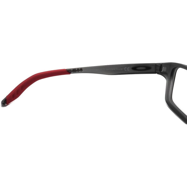 May include: Gray and red sunglasses with a red rubber temple arm. The sunglasses have a black frame and a clear lens. The text "Oakley" and "Made in China" are printed on the frame.