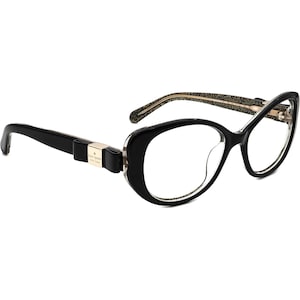 Puede incluir: Gafas de vista negras de estilo ojo de gato con un detalle de purpurina dorada en las patillas y un lazo negro con el texto "kate spade new york" en el lado izquierdo.