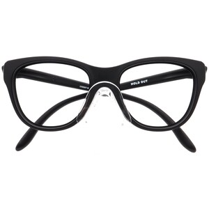 May include: Black eyeglasses with a cat-eye shape. The frames are matte black, and the lenses are clear. The nose pads are transparent. The text "HOLD OUT" is printed on the right arm of the glasses.