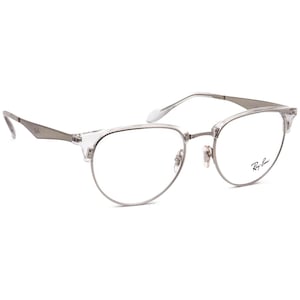 Peut inclure: Lunettes à monture transparente avec une barre frontale et des branches en métal argenté. Les verres sont transparents et le logo Ray-Ban est visible sur la lentille droite. Design classique et semi-cerclé.