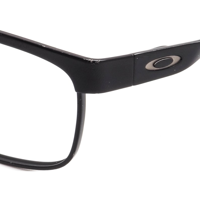 K&ouml;nnte beinhalten: Schwarze rechteckige Brille mit einem silbernen Oakley-Logo an der Seite.
