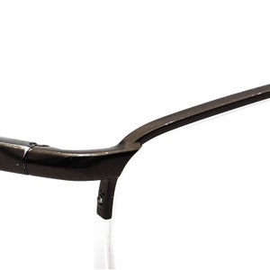 May include: Close-up of the black metal frame of a pair of eyeglasses. The frame is curved and has a smooth finish.
