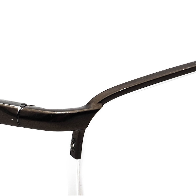 May include: Close-up of the black metal frame of a pair of eyeglasses. The frame is curved and has a smooth finish.