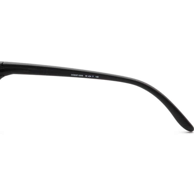 May include: Black sunglasses arm with the text "OO9357-0555 55 17 145". The arm curves downward and has a matte finish. The sunglasses appear to be made of a durable material.