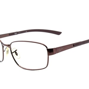 Puede incluir: Gafas de metal de color marrón con lentes transparentes. El nombre de la marca "Ray-Ban" es visible en la patilla derecha.