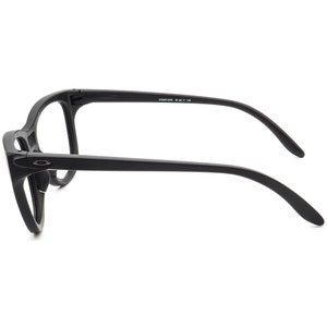 May include: Black eyeglasses with a matte finish. The glasses have a thick frame and curved temples. The Oakley logo is visible on the side of the frame. The text "OO9287-0855 55 17 145" is printed on the temple.