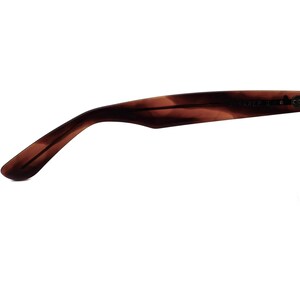 Może przedstawiać: Zbliżenie na brązową, ż&oacute;łwiową zausznicę okular&oacute;w przeciwsłonecznych. Na zauszniku widnieje napis "Ray-Ban II C".
