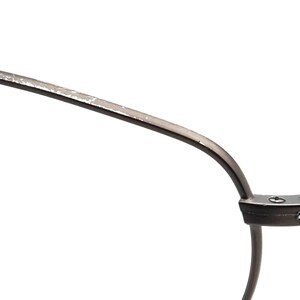 May include: Close-up of a pair of eyeglasses with a dark metal frame. The frame has a curved design with a silver-colored finish on the top edge. The glasses are set against a white background.
