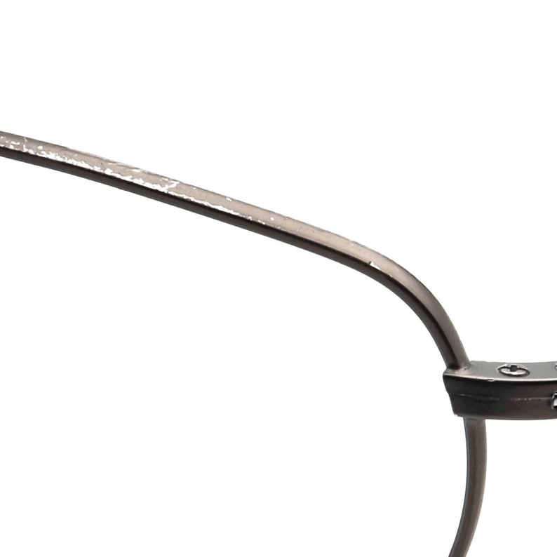 May include: Close-up of a pair of eyeglasses with a dark metal frame. The frame has a curved design with a silver-colored finish on the top edge. The glasses are set against a white background.