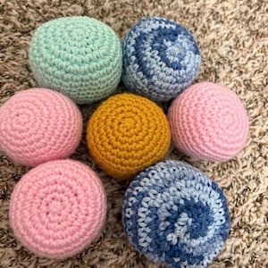 Pode incluir: Uma coleção de sete esferas de crochê em várias cores. As esferas incluem tons de rosa, azul, amarelo e verde. Os itens feitos à mão são dispostos em um padrão circular.