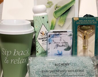 May include: A green and white gift box filled with bath and beauty products. The box contains a green and white hand cream, a green and white face mask, a green and white bath salt, a green and white jade roller, and a green and white tumbler with the text "Sip back & relax".