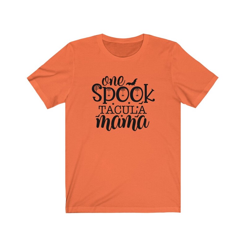 K&ouml;nnte beinhalten: Orangefarbenes T-Shirt mit dem schwarzen Schriftzug &bdquo;one spooktacular mama&ldquo;. Das Wort &bdquo;spook&ldquo; ist mit einer Fledermaus und einem Spinnennetz verziert. Das T-Shirt hat einen Rundhalsausschnitt und kurze &Auml;rmel.