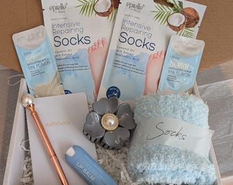May include: A gift box filled with self-care items. Includes two packets of foot repair socks, two packets of exfoliating scrub, a light blue fluffy pair of socks, a pen, a notebook, a hair clip, and a lip balm.