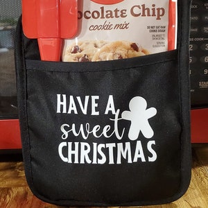 May include: Black oven mitt with white text that says "Have a sweet Christmas" and a gingerbread man graphic. A red spatula and a Betty Crocker chocolate chip cookie mix package are in the pocket of the oven mitt.