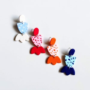 May include: Four pairs of geometric dangle earrings with abstract patterns. The earrings are made of polymer clay and feature a variety of colours, including blue, red, orange, and white.