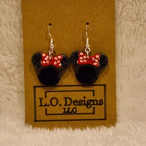 May include: A pair of black and red glitter Minnie Mouse earrings with white polka dots on the bow. The earrings are on a brown card with the text "L.O. Designs LLC".