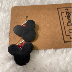 May include: A pair of black Mickey Mouse head shaped earrings with silver hooks. The earrings are on a brown card with the text "10 Designs" printed on it.