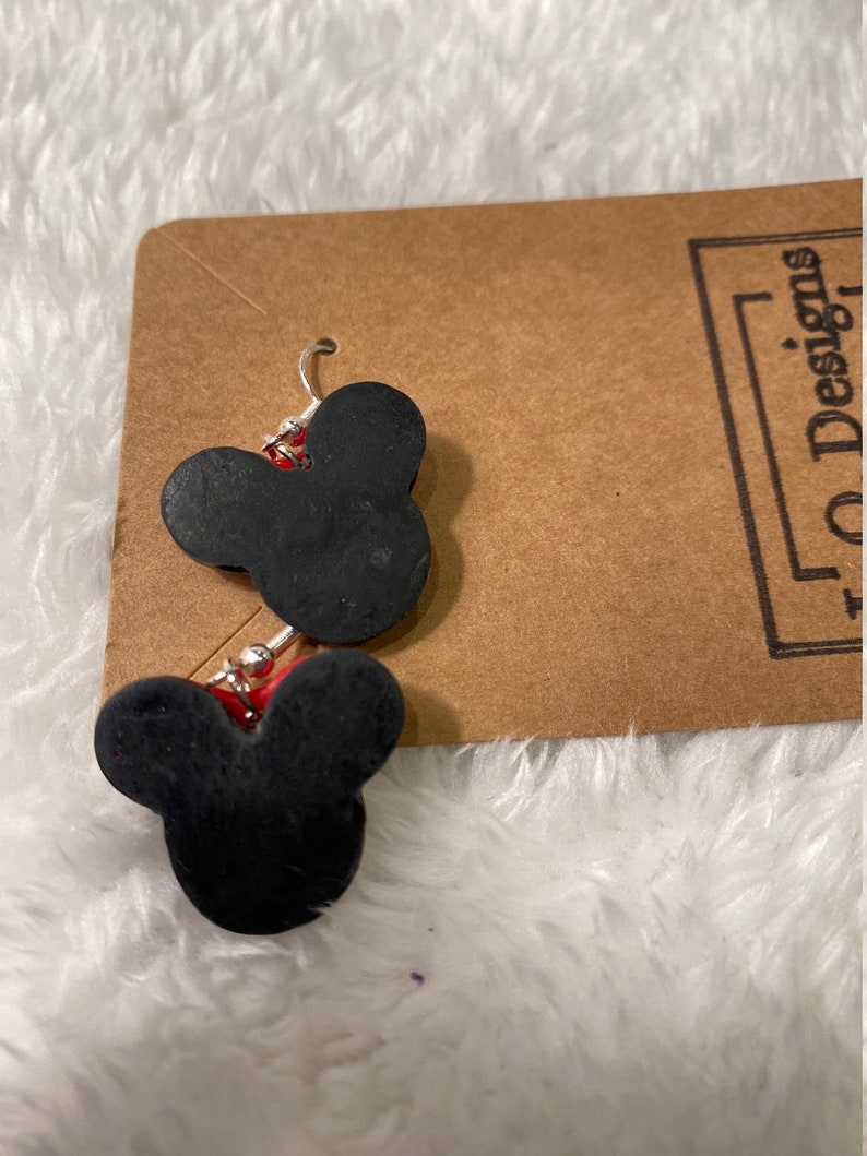 May include: A pair of black Mickey Mouse head shaped earrings with silver hooks. The earrings are on a brown card with the text "10 Designs" printed on it.