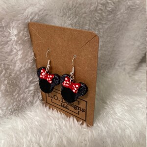 May include: A pair of black and red Minnie Mouse earrings with white polka dots. The earrings are on a brown card with the text "L.O. Designs LLC".
