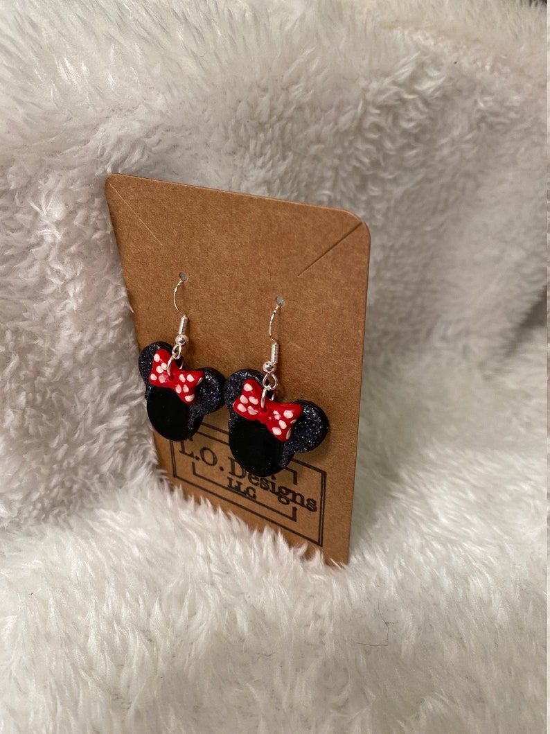 May include: A pair of black and red Minnie Mouse earrings with white polka dots. The earrings are on a brown card with the text "L.O. Designs LLC".